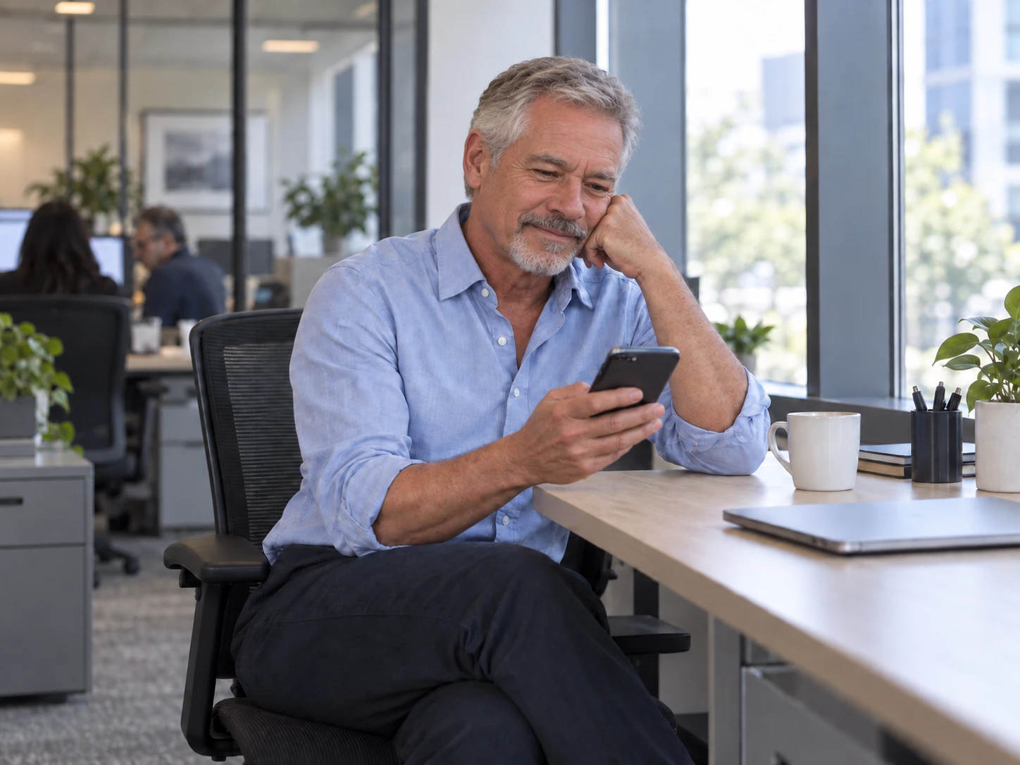 A finance lead at a desk in a bright office, smiling at a phone, laptop closed.