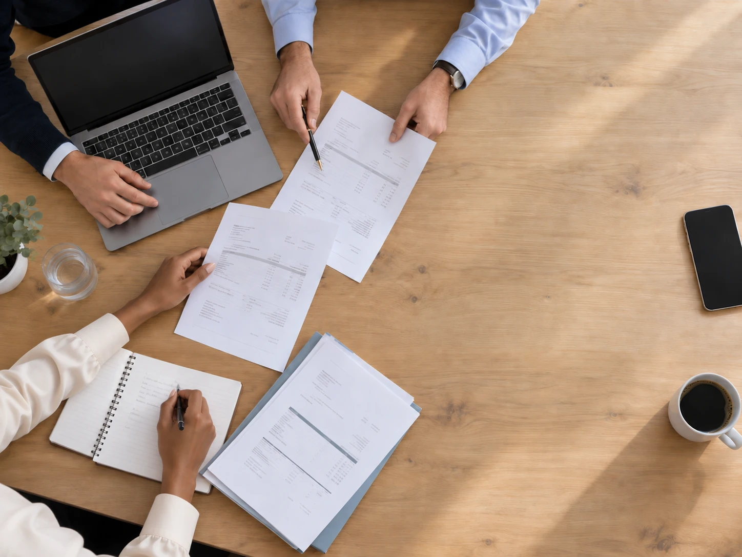 Overhead view of a table where the Listra AP team works through invoices with a laptop, notes and a pen, while a phone and a coffee sit on the clear side of the table.